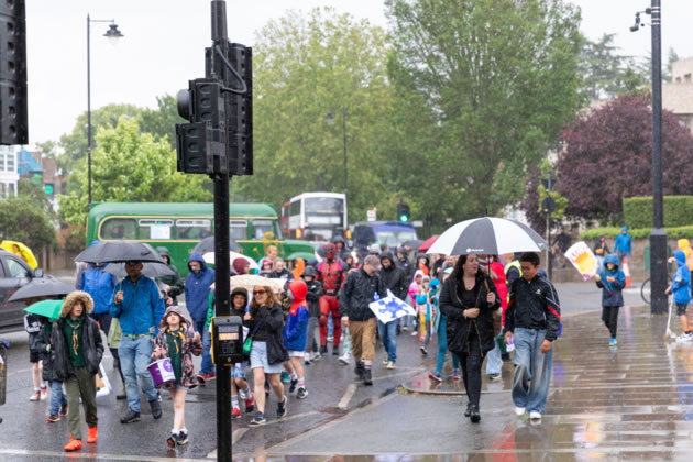 A superhero is undeterred by the rain and joins the procession 